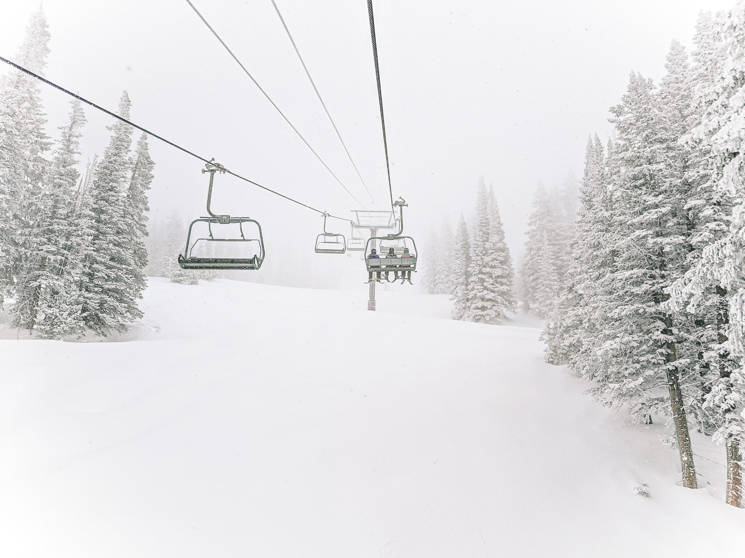 Three skiers sit on a chairlift, over a snowy slope at Steamboat