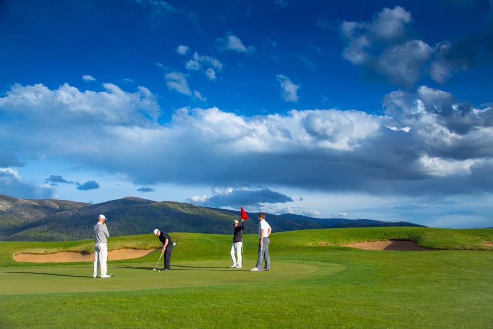 Four men enjoying a round of golf against a backdrop of majestic mountains.