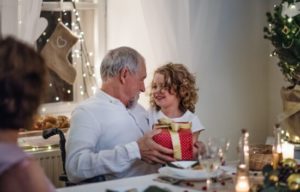 Young girl giving a red and gold wrapped gift box to an older gentleman.