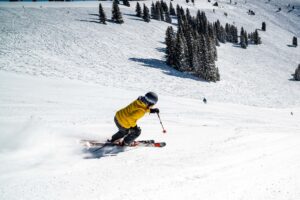 A skiier in a yellow jacket speeds down the mountain