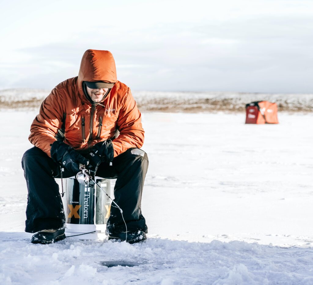 A man in an orange jacket ice fishing