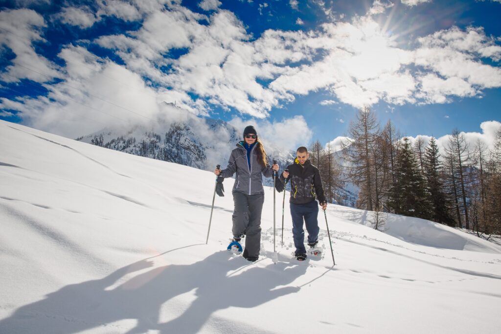 Two people snowshoeing, backdropped by a bright blue sky
