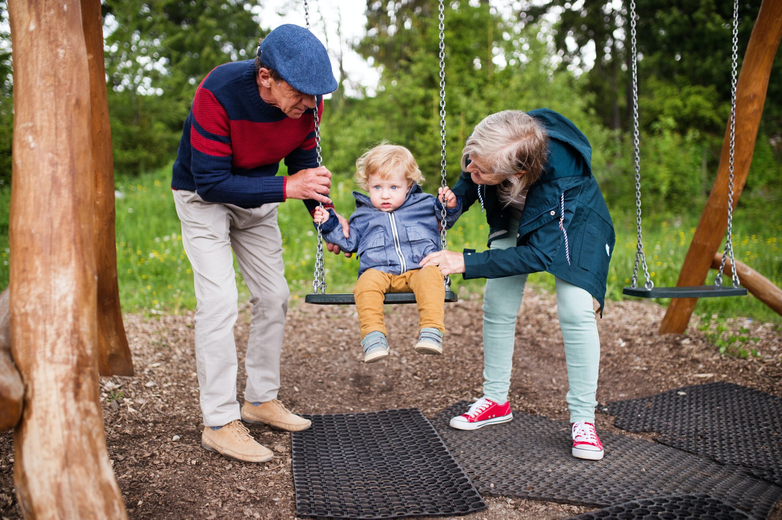 Two grandparents push a baby on a swing