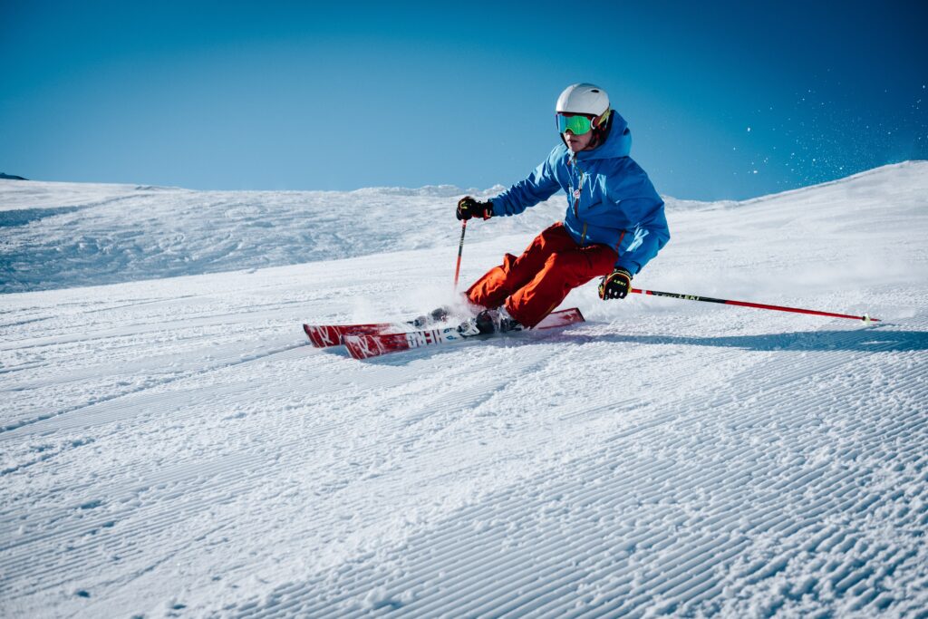 A skier speeds down a snowy slope against a clear blue sky