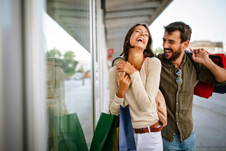 A couple laugh while carrying colorful paper shopping bags
