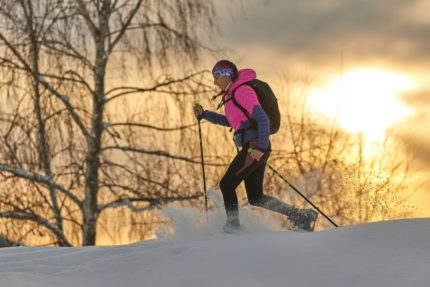 A snow-shoer walks in front of a sunset