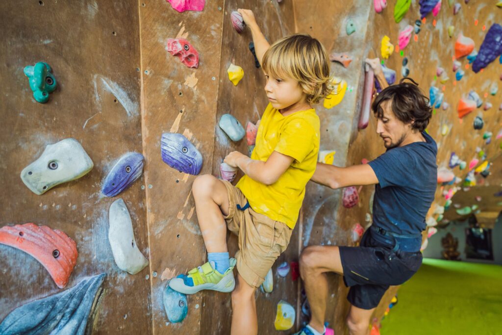 A child and his father climbing a bouldering wall