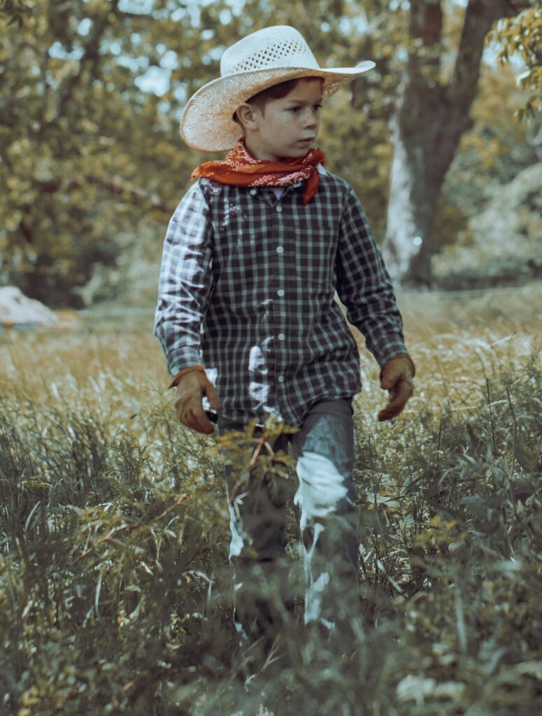 A cowboy child walks through a field