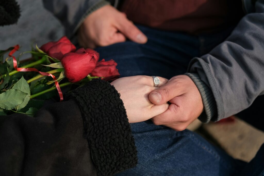 A couple hold hands with red roses resting on their lap
