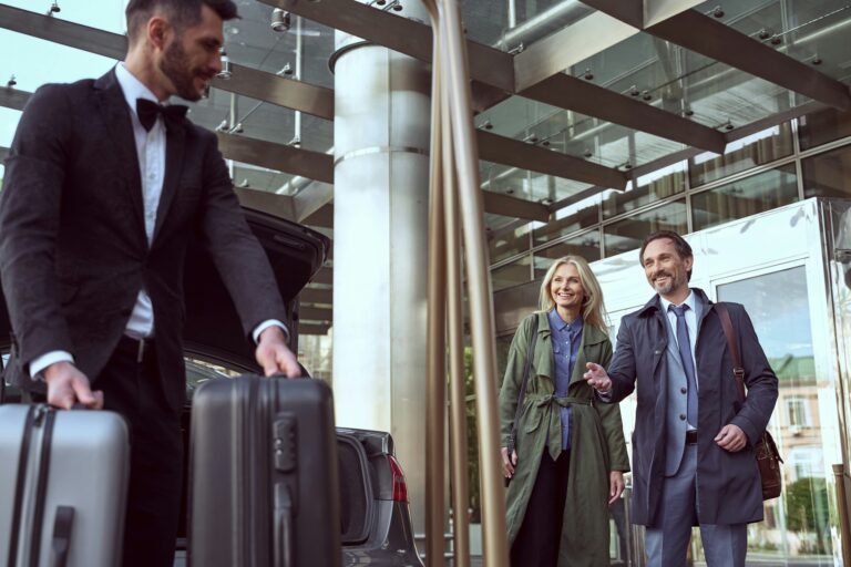 A couple smile at a concierge who is carrying their luggage