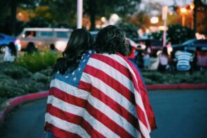 Two women with the stars and stripes flag draped around them