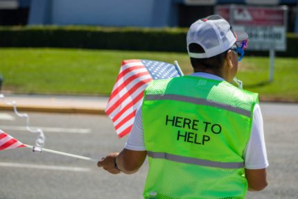 A volunteer in a high-visibility vest that says 'here to help'