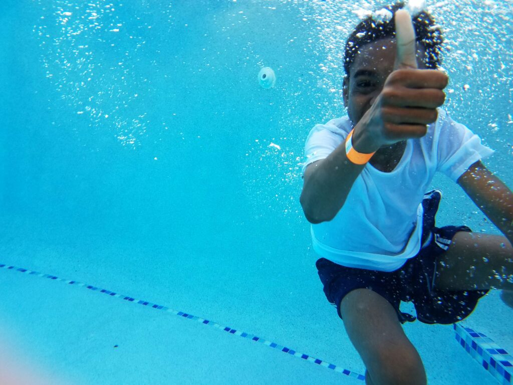 A child swimming underwater, giving a thumbs up
