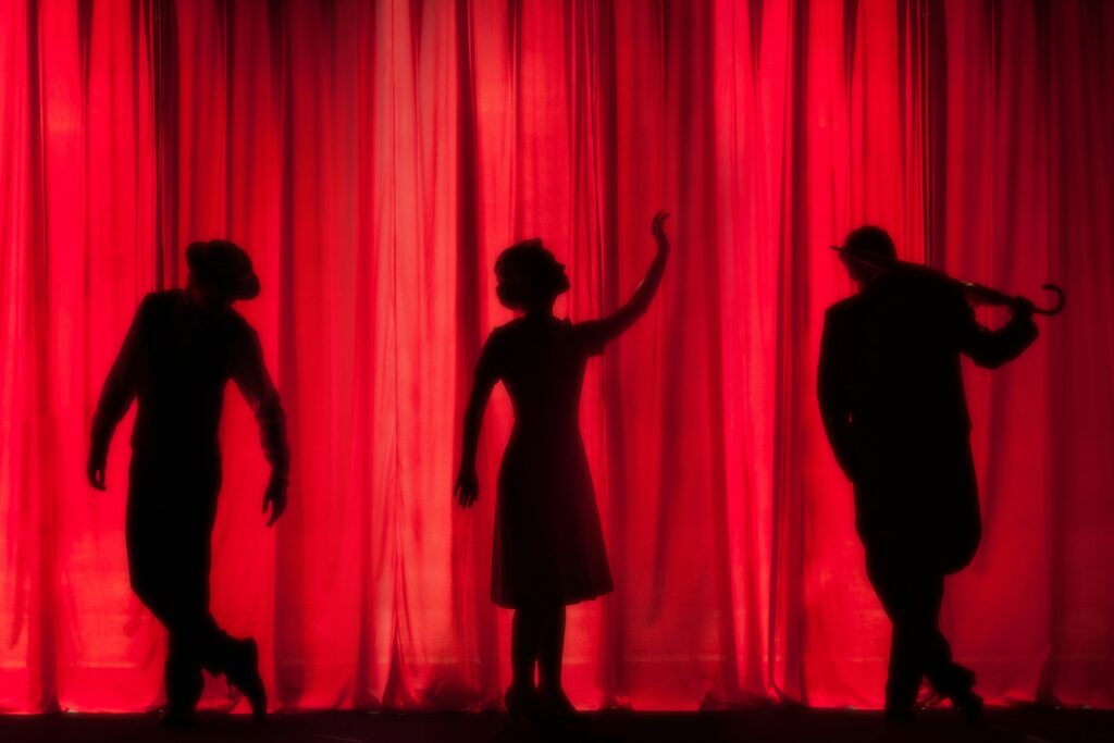 Three silhouettes of actors in front of a red curtain