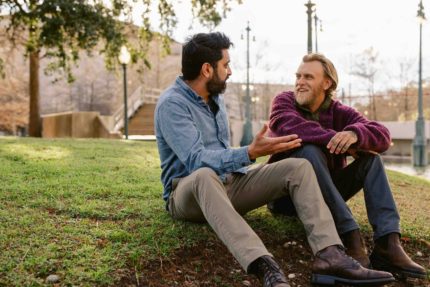 Two men chatting while sat on grass