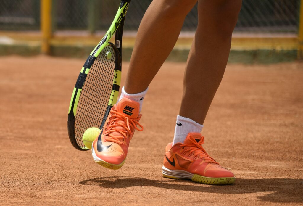 Feet in orange sneakers with a tennis racket and tennis ball