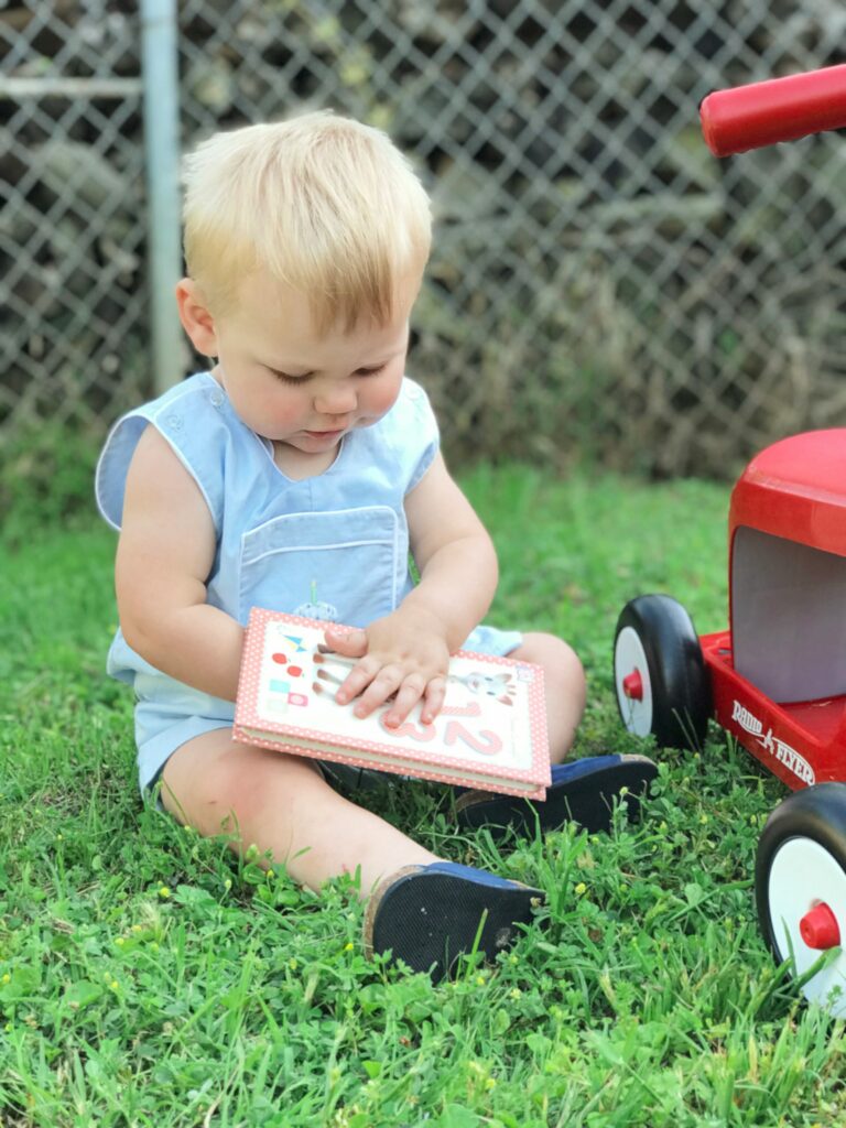 A baby holding a book in the grass