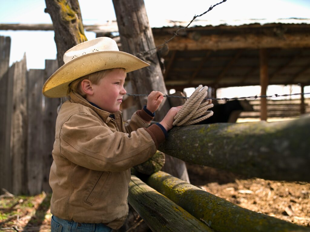 A child cowboy looking over a fence