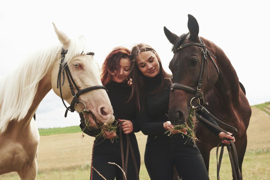 Two women feeding horses grass