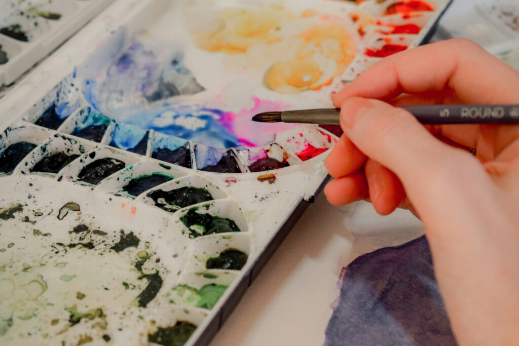 A hand dipping a paintbrush into watercolors