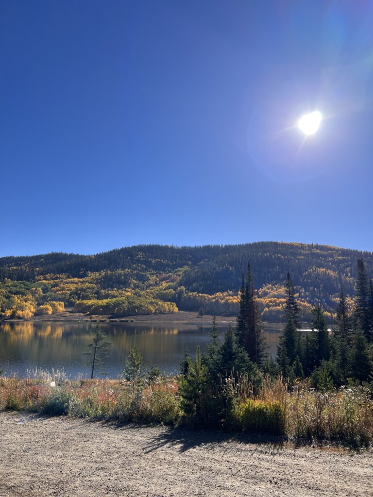 View across a lake, looking out to a valley and mountain covered with trees with yellow and green leaves.