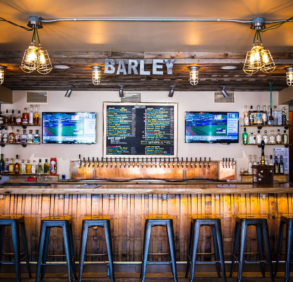 The bar at The Barley Tap and Tavern. Barstool seats, and wooden bar, and a large list of draft beer and cocktails in Steamboat Springs.