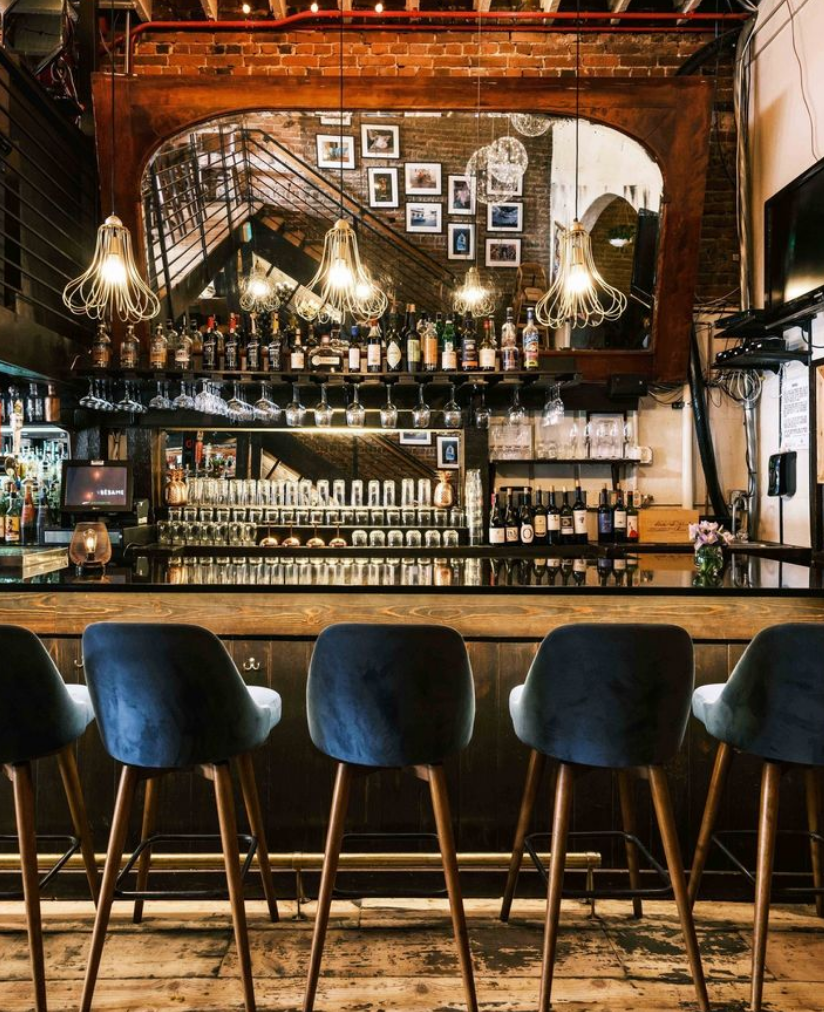 The bar at Besame, Dark colors, lush blue barstools, and liquor bottles on the wall. They are known for their cocktails in Steamboat Springs.