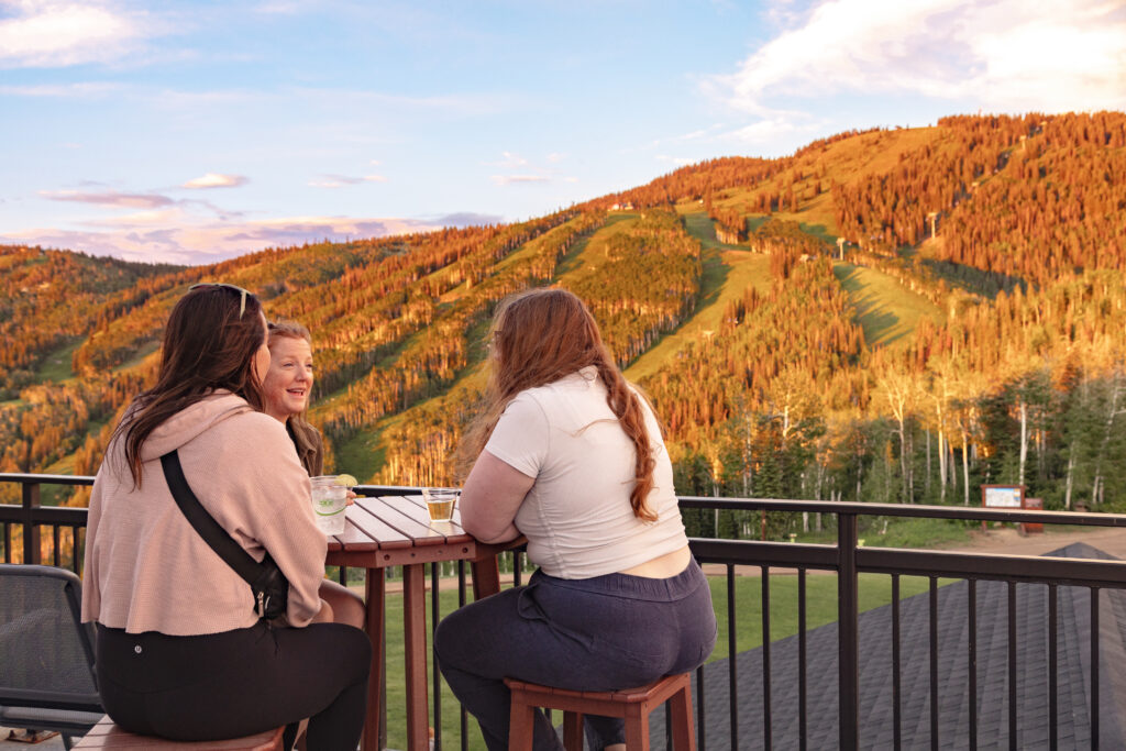 Three women talking at a high top table overlooking the golden leaves of the aspens in Steamboat Springs at sunset