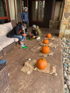 Three people setting out pumpkins to carve on an outside porch. There are great places to find pumpkins in Steamboat Springs.