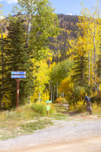 The entrance to a hiking trail at Steamboat resort in Steamboat Springs. Trees surround the sign with green and yellow leaves.