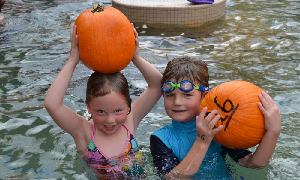 Two children holding up pumpkins in a swimming pool. Part of the Pumpkin Float event in Steamboat Springs.