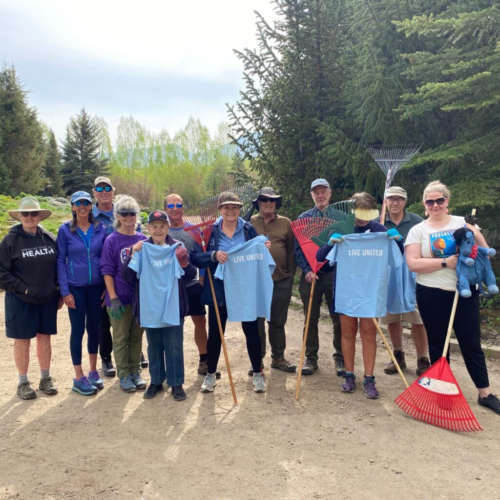 A group of gardening volunteers holding rakes and other gardening tools at the Yampa River Botanic Park. 