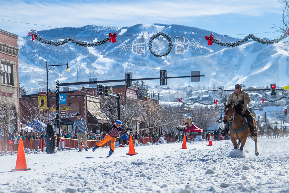 Man on horseback pulling a child on skis along the main street as part of an event during the Steamboat Winter Carnival