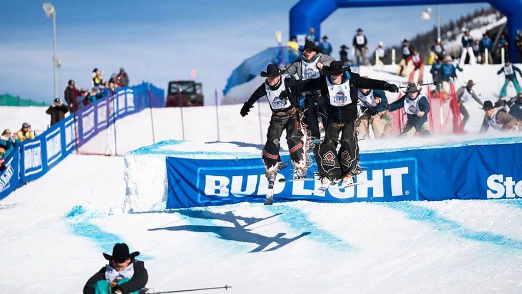 A group of 3 skiers jumping during the Stampede portion of the Cowboy Downhill - a annual January event in Steamboat Springs.