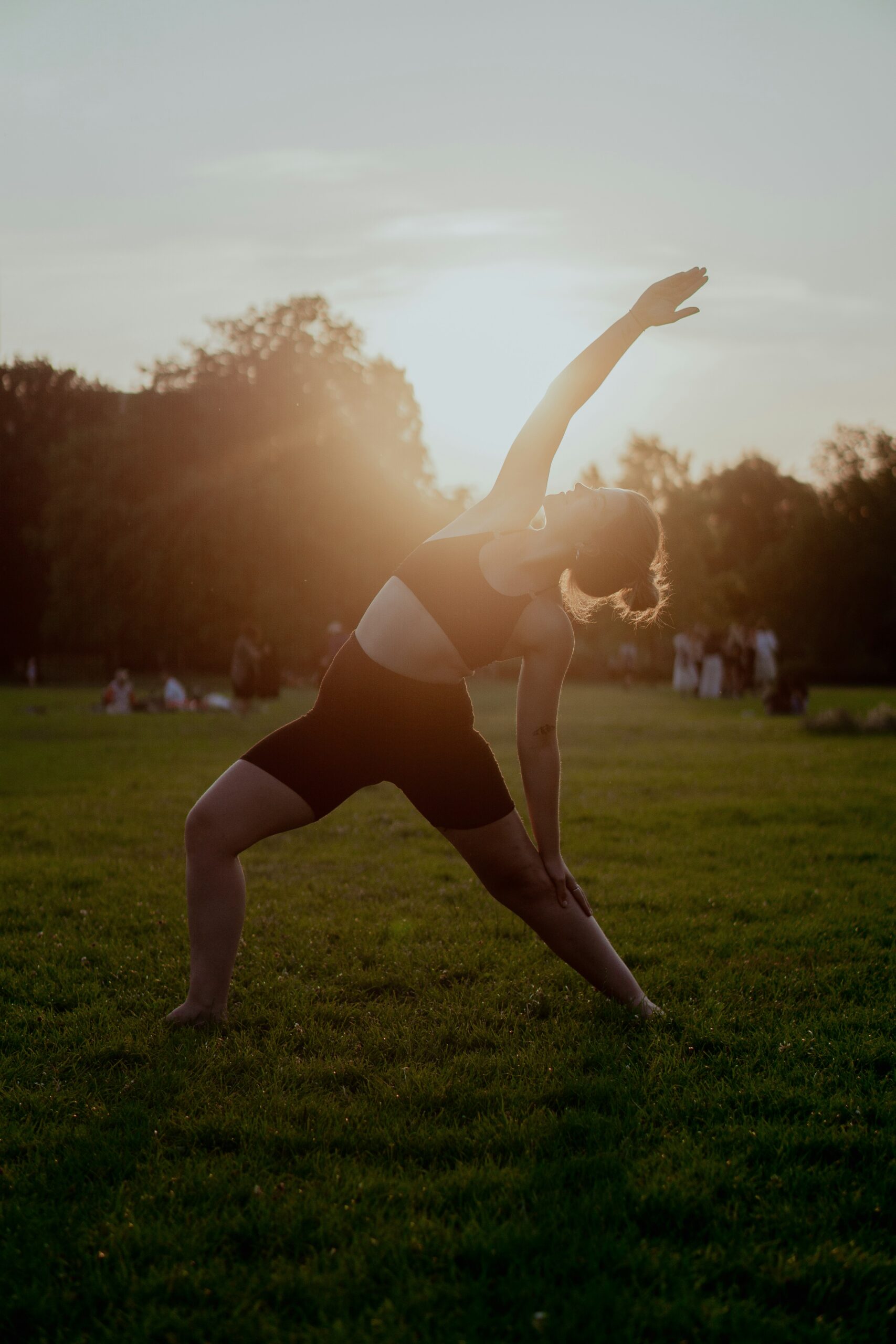 Women stretching upwards in a yoga pose with the sunset behind her.