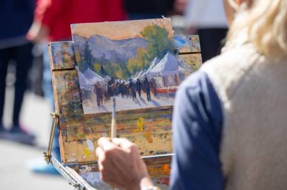 View over woman's shoulder as she paints a mountain landscape on canvas.