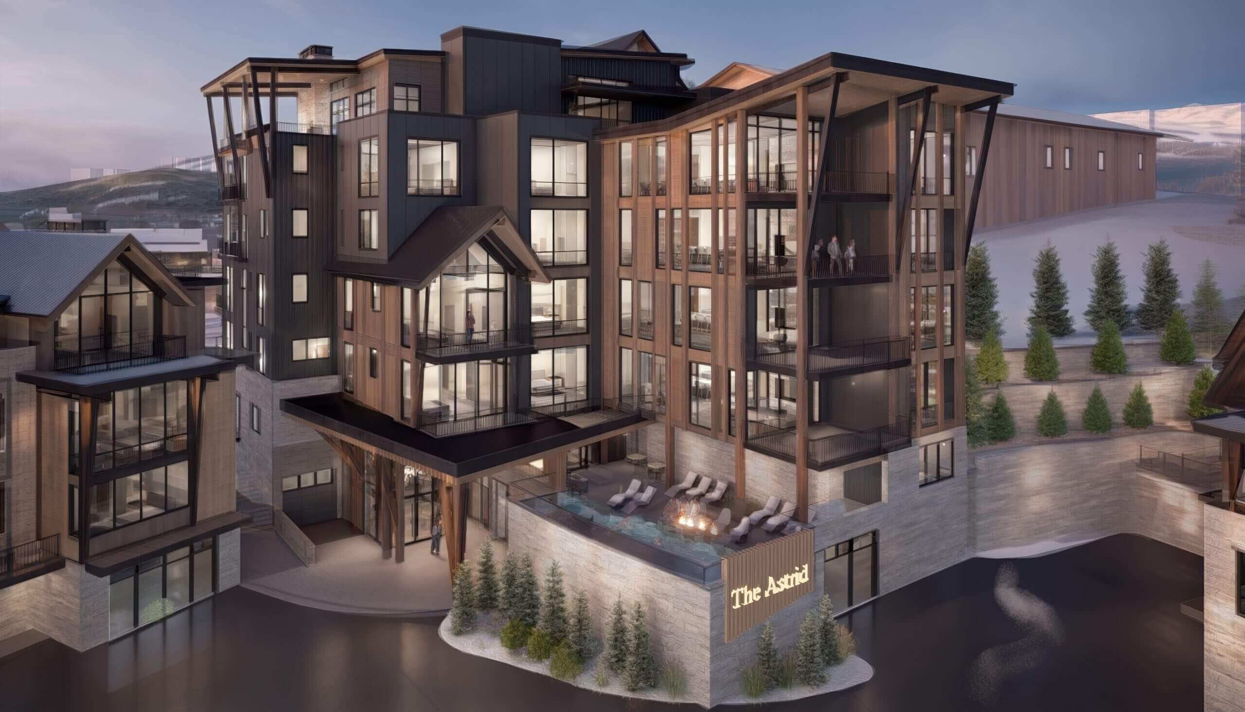 Exterior view of The Astrid luxury mountain residences with balconies, warm interior lighting, and a terrace overlooking an alpine landscape.