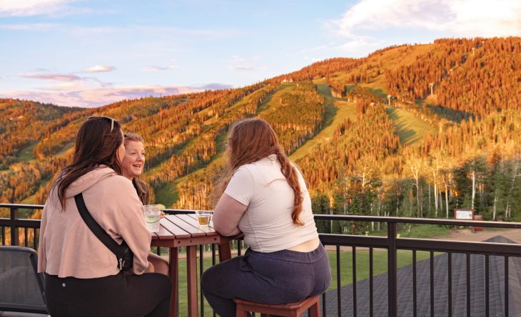 Three women talking at a high top table overlooking the golden leaves of the aspens in Steamboat Springs at sunset