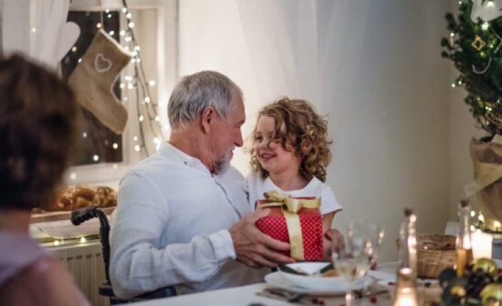 Young girl giving a red and gold wrapped gift box to an older gentleman.