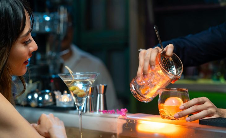 A woman watching as a cocktail is poured into a glass from a shaker.