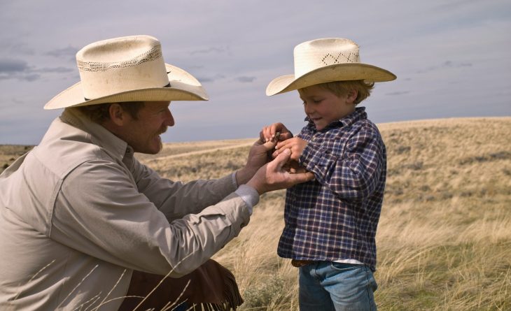 A father and a little boy holding hands and waering cowboy hats.