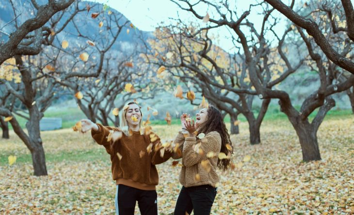 Two friends in the fall, throwing colored leaves in the air